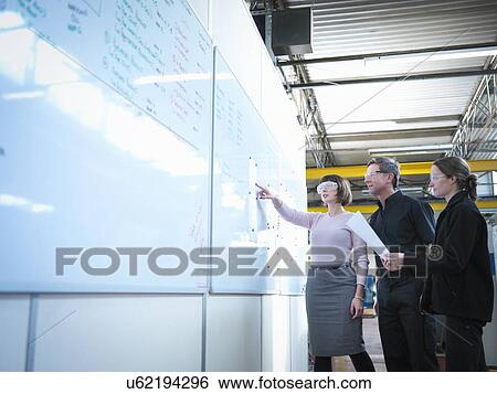 Stock Photograph - Workers in whiteboard meeting in engineering factory. Fotosearch