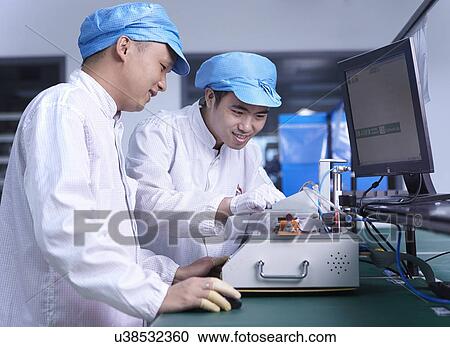 Stock Image - Workers using machinery in factory that specialises in creating functional circuits on flexible surfaces. Fotosearch