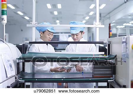 Stock Image - Workers using machinery in factory that specialises in creating functional circuits on flexible surfaces. Fotosearch