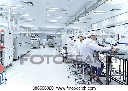 Stock Image - Workers using microscopes in factory that specialises in creating functional circuits on flexible surfaces. Fotosearch