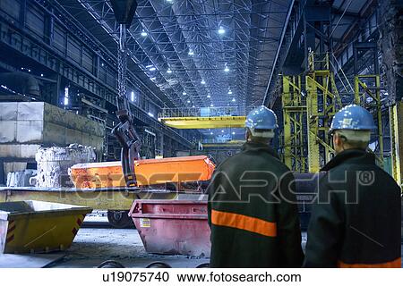Stock Image - Workers watch red hot steel in furnace in steelworks. Fotosearch
