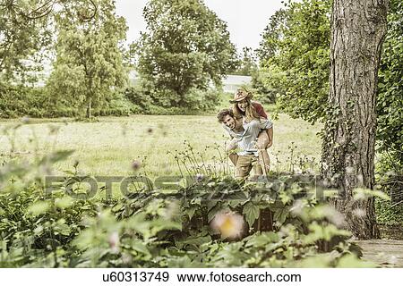 "Young couple in garden, man giving woman piggyback" View Large Photo Image Stock Photo - "Young couple in garden, man giving woman piggyback". Fotosearch