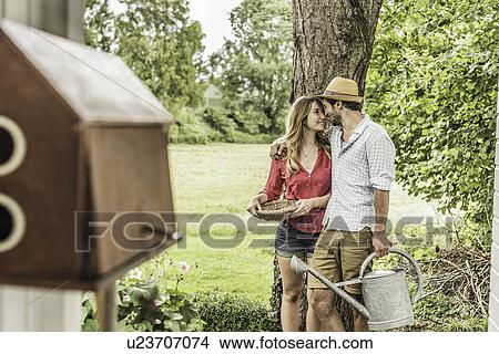 Picture - "Young couple in garden, man with watering can". Fotosearch