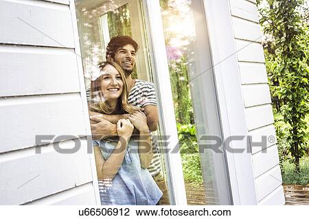Stock Image - Young couple looking out of patio window. Fotosearch