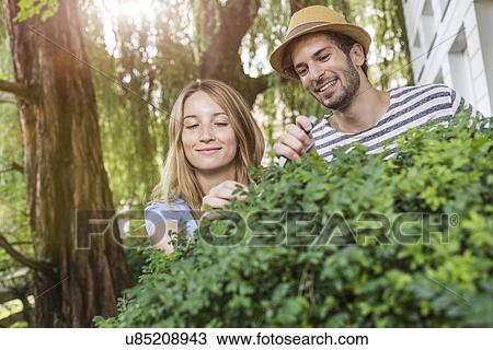 Stock Image - Young couple pruning bush in garden. Fotosearch