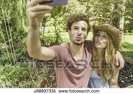 Stock Photography - Young couple taking selfie with cell phone in garden. Fotosearch