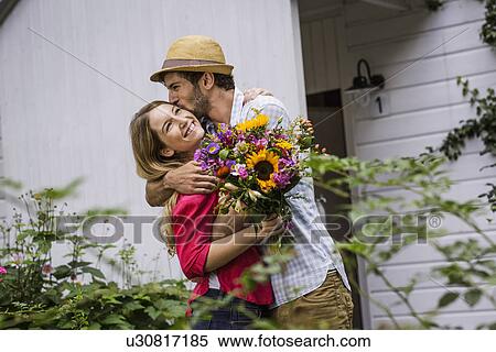 Stock Photography - Young couple with bunch of flowers hugging in garden. Fotosearch