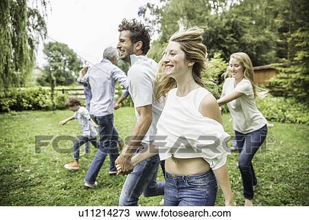 Stock Image - Young man and woman running in garden with family. Fotosearch
