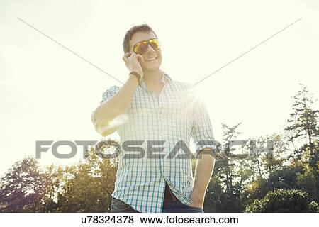 Young man chatting on smartphone in park View Large Photo Image Stock Photo - Young man chatting on smartphone in park. Fotosearch