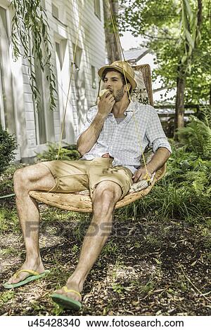 Young man eating apple sitting on hammock in garden View Large Photo Image Stock Image - Young man eating apple sitting on hammock in garden. Fotosearch