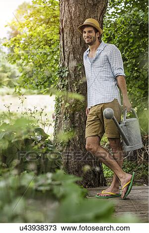 Young man leaning against tree in garden with watering can View Large Photo Image Stock Image - Young man leaning against tree in garden with watering can. Fotosearch