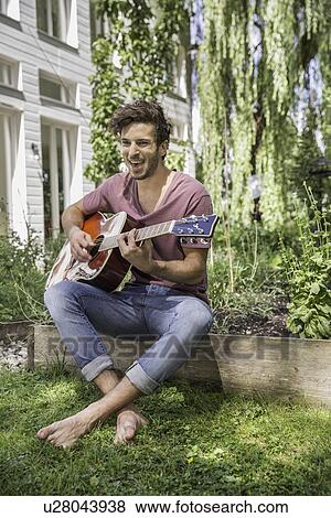 Stock Photo - Young man playing guitar in garden. Fotosearch