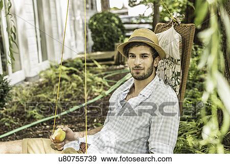 Stock Photo - Young man sitting on hammock in garden. Fotosearch