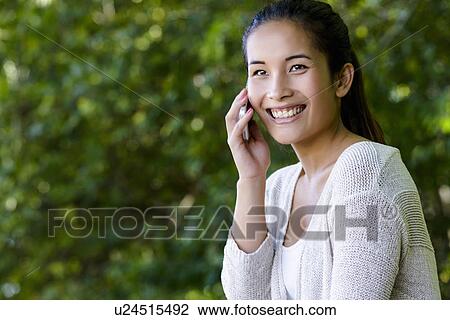 Young woman chatting on smartphone in park View Large Photo Image Stock Image - Young woman chatting on smartphone in park. Fotosearch