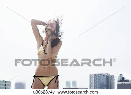 Stock Photo - Young woman in gold bikini with hair blowing in breeze on rooftop. Fotosearch