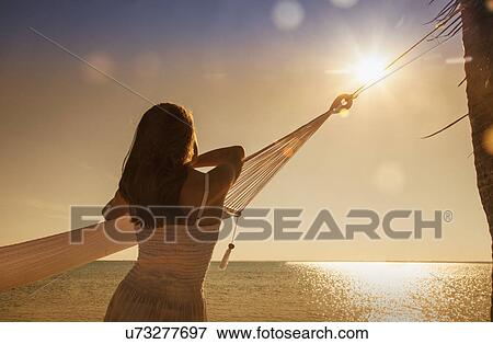 "Young woman leaning on hammock looking at sunset over sea, Etosha National Park, Namibia" View Large Photo Image Stock Photo - "Young woman leaning on hammock looking at sunset over sea, Etosha National Park, Namibia". Fotosearch