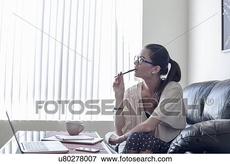 Stock Photo - Young woman on sofa biting pencil. Fotosearch