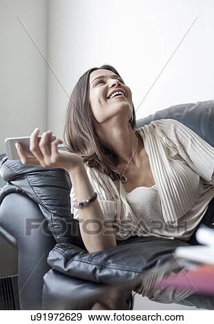 "Young woman on sofa with smartphone, laughing" View Large Photo Image Stock Photo - "Young woman on sofa with smartphone, laughing". Fotosearch