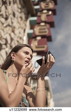 Stock Photo - "Young woman, outdoors, looking in compact mirror, low angle view". Fotosearch