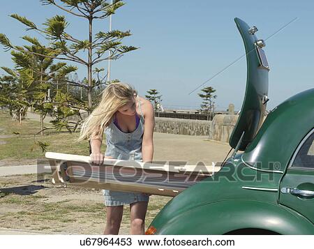 Stock Image - "Young woman removing deck chair from car boot at beach, Altona, Melbourne, Victoria, Australia". Fotosearch