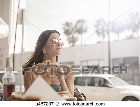 "Young woman sitting at outdoor table, eating sandwich" View Large Photo Image Stock Image - "Young woman sitting at outdoor table, eating sandwich". Fotosearch