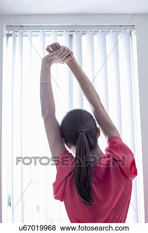 Young woman stretching whilst looking out of apartment window View Large Photo Image Stock Photo - Young woman stretching whilst looking out of apartment window. Fotosearch