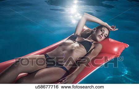 Stock Photograph - "Young woman sunbathing on inflatable in swimming pool, Cagliari, Sardinia, Italy". Fotosearch