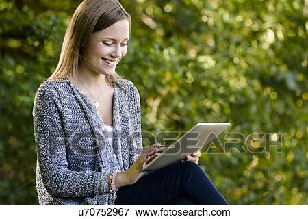 Stock Photo - Young woman using touchscreen on digital tablet in park. Fotosearch