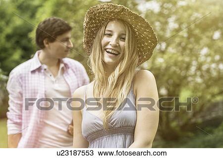 Stock Image - "Young woman wearing straw hat laughing, portrait". Fotosearch