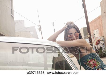 "Young woman wearing sunglasses, leaning against car" View Large Photo Image Stock Image - "Young woman wearing sunglasses, leaning against car". Fotosearch