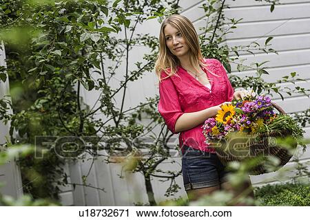Stock Image - Young woman with basket of flowers in garden. Fotosearch