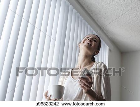 Stock Image - Young woman with smartphone laughing. Fotosearch