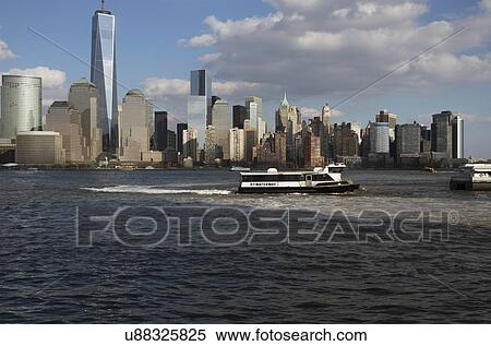 Stock Photography - "From New Jersey, a water taxi is seen in front of New York City Skyline featuring One World Trade Center (1WTC), Freedom Tower, New York City, New York, USA". Fotosearch