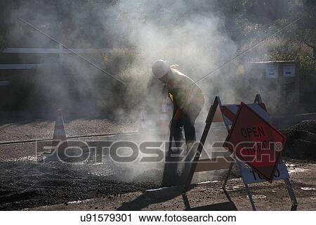 Stock Image - "Roadworker repaves road with steam, Encino Drive, Oak View, California, USA". Fotosearch