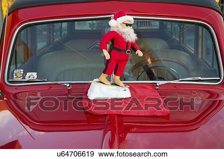 Stock Photo - "Surfing Santa Clause on a vintage red car hood, California, USA". Fotosearch