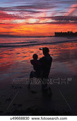 "Woman with child takes picture of purple and orange sunset looking towards Anacapa Island, Ventura, California, USA" View Large Photo Image Stock Image - "Woman with child takes picture of purple and orange sunset looking towards Anacapa Island, Ventura, California, USA". Fotosearch