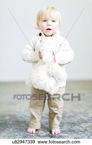 Stock Photo - Boy (2-3) holding toy dog standing on floor. Fotosearch