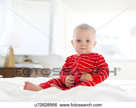 Stock Photograph - Boy (2-3) in striped pajamas sitting on bed. Fotosearch
