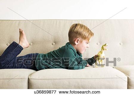 Stock Photo - Boy (2-3) playing with toy dinosaur on sofa. Fotosearch
