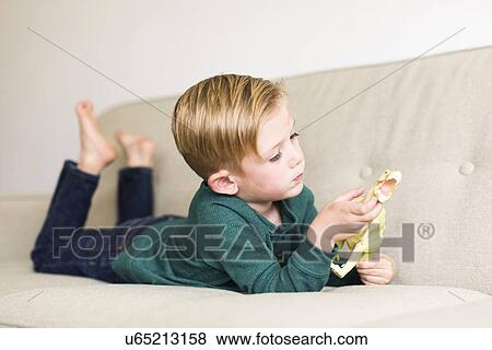 Boy (2-3) playing with toy dinosaur on sofa View Large Photo Image Stock Photo - Boy (2-3) playing with toy dinosaur on sofa. Fotosearch