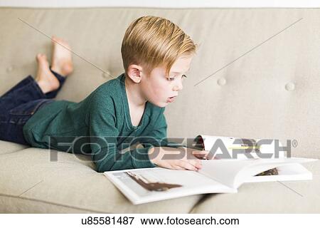 Stock Photo - Boy (2-3) reading book on sofa. Fotosearch