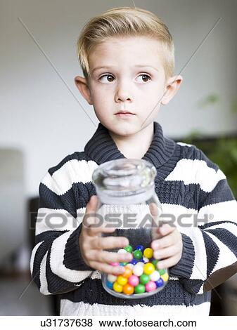Stock Photo - Boy (6-7) holding glass jar with candies. Fotosearch