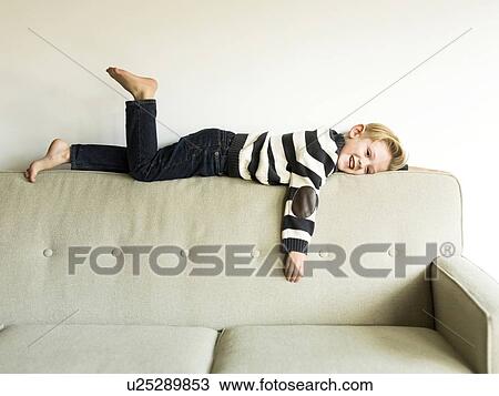 Stock Image - Boy (6-7) lying on sofa. Fotosearch