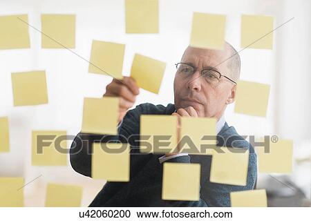 Stock Image - Businessman arranging adhesive notes on glass wall. Fotosearch