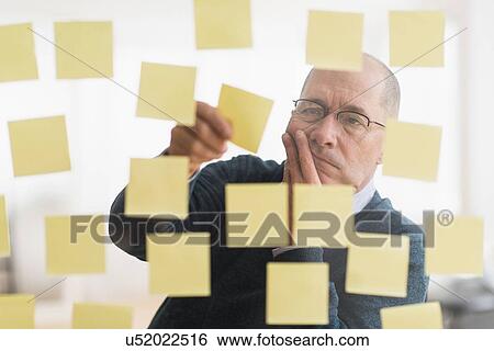 Businessman arranging adhesive notes on glass wall View Large Photo Image Stock Photograph - Businessman arranging adhesive notes on glass wall. Fotosearch