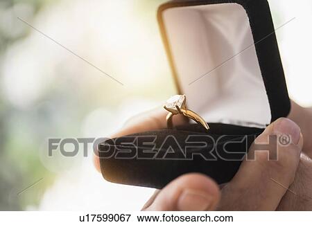 Close up of man's hand holding open box with engagement ring View Large Photo Image Stock Photo - Close up of man's hand holding open box with engagement ring. Fotosearch