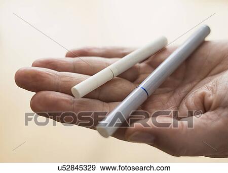 Stock Photo - Close up of man's hand holding cigarette and e-cigarette. Fotosearch