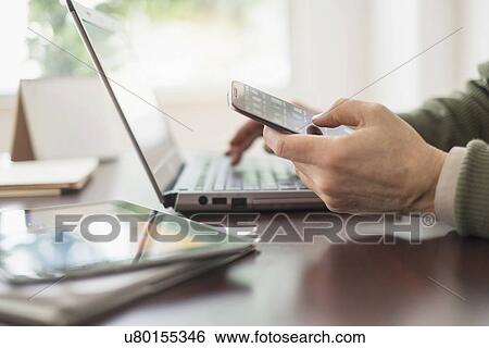 Stock Photograph - Close up of man's hands working at desk with electronic devices. Fotosearch