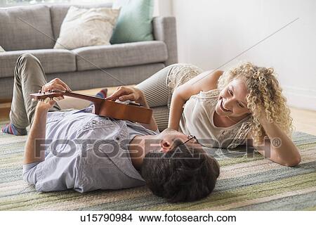 Picture - Couple lying on floor playing ukulele. Fotosearch