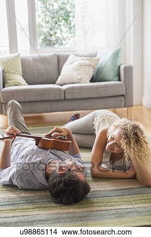 Picture - Couple lying on floor playing ukulele. Fotosearch